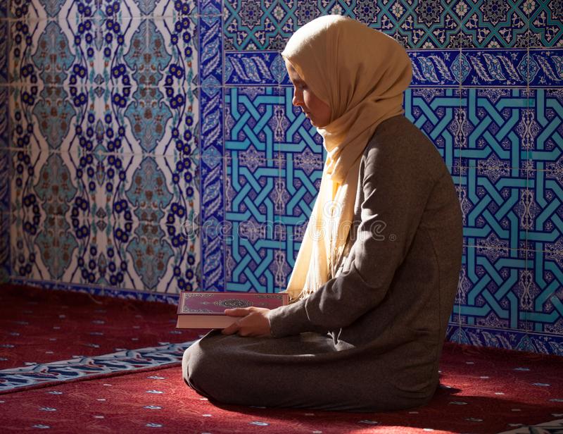 Young Muslim woman reads Quran under sunlight .